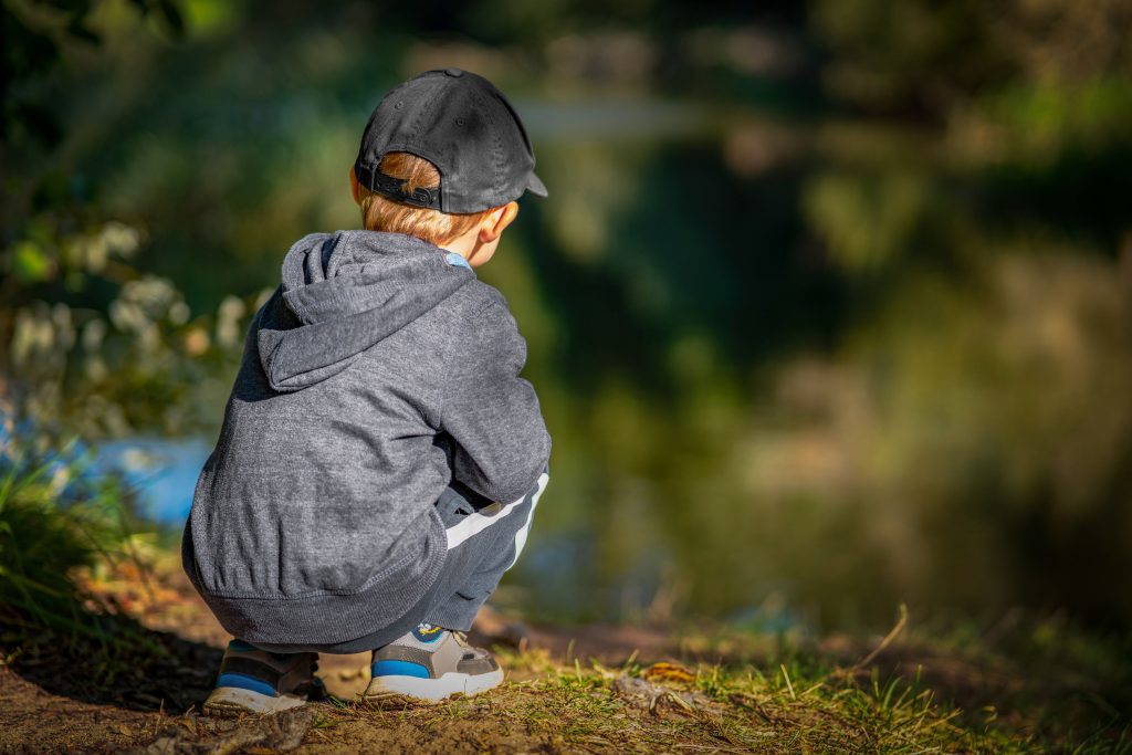 Enfant accroupi dans la nature, devant un étang. Mouvement instinctif et naturel.