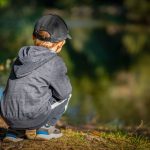 Enfant accroupi dans la nature, devant un étang. Mouvement instinctif et naturel.